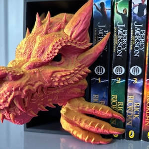 A decorative dragon bookend holding multiple books, adding a whimsical touch to a bookshelf filled with literary treasures.