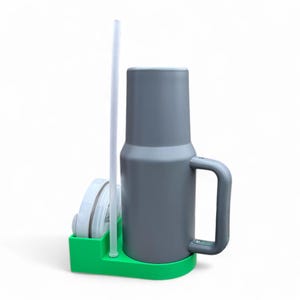 May include: A gray travel mug with a handle and a clear plastic straw, sitting in a green holder with a white lid.