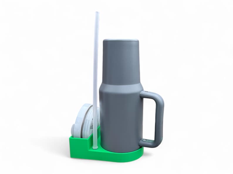 May include: A gray travel mug with a handle and a clear plastic straw, sitting in a green holder with a white lid.