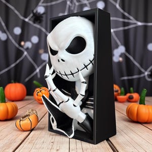 May include: A white and black Jack Skellington figure in a black box, with a thoughtful expression. The figure is surrounded by orange pumpkins, creating a Halloween theme.