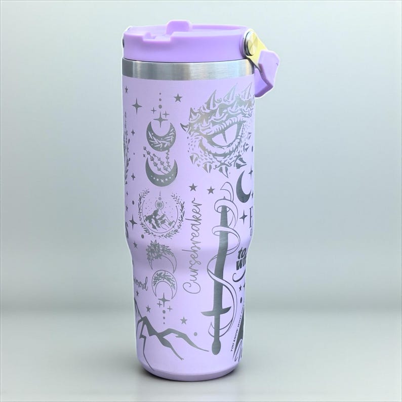 May include: A lilac insulated travel mug with a matching lid and handle. The mug features celestial and fantasy-themed designs, including moons, stars, and a sword. The text "Cursebreaker" is printed on the side.