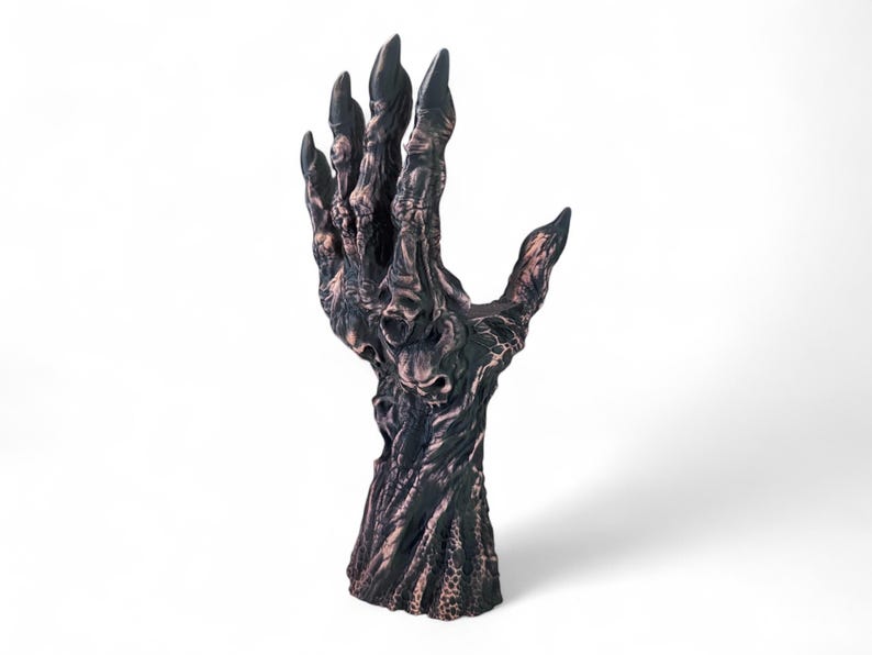 May include: A dark, textured sculpture of a hand with long, sharp fingernails. The hand is a mix of dark brown and bronze colors, with a detailed, almost skeletal appearance. The fingers are spread, and the palm is open.