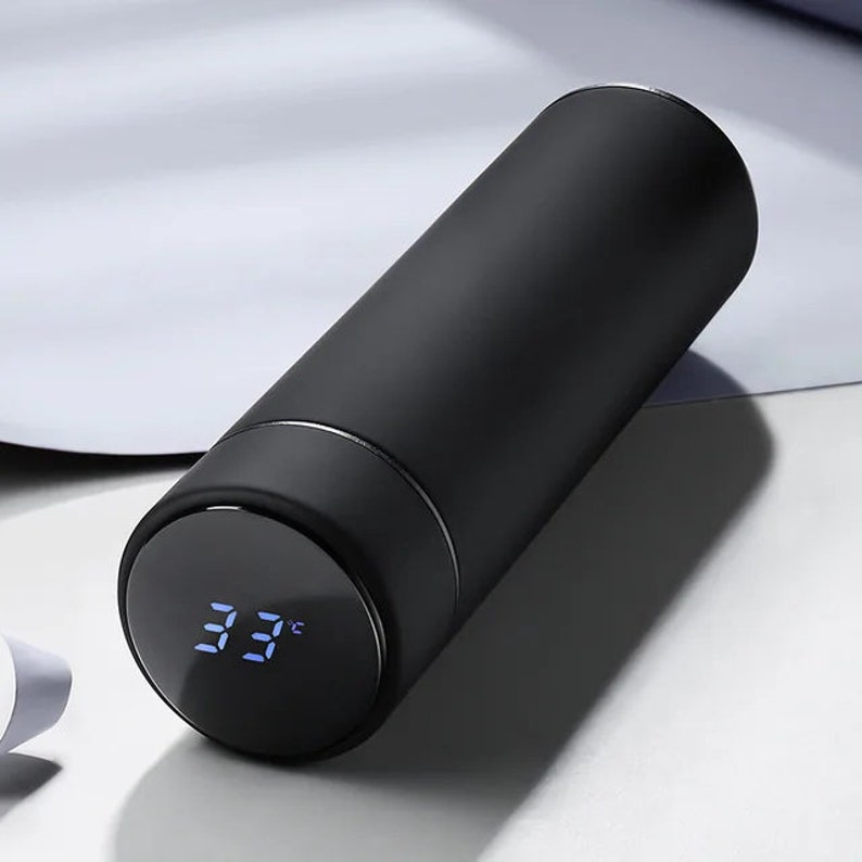 A black cylindrical thermos with a digital temperature display showing 33°C on its lid, placed on a white surface.