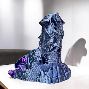 May include: A 3D printed dragon tower dice holder with a blue and purple metallic finish. The tower has a dragon wrapped around it and a winding path leading up to the top.