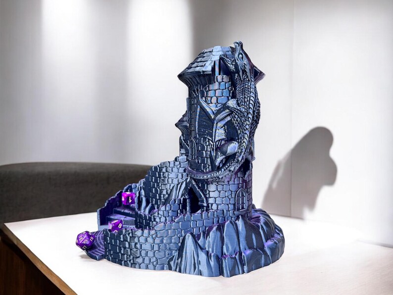 May include: A 3D printed dragon tower dice holder with a blue and purple metallic finish. The tower has a dragon wrapped around it and a winding path leading up to the top.