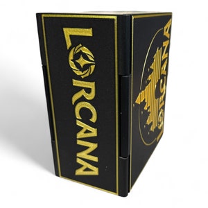May include: Black box with gold lettering that reads "LORCANA" and a gold design on the side.