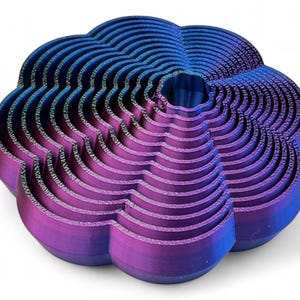 May include: A 3D-printed, abstract sculpture in shades of blue and purple. The object has a layered, wave-like design, with a central opening. The colour gradient shifts from blue at the top to purple at the bottom. The sculpture is on a white background.