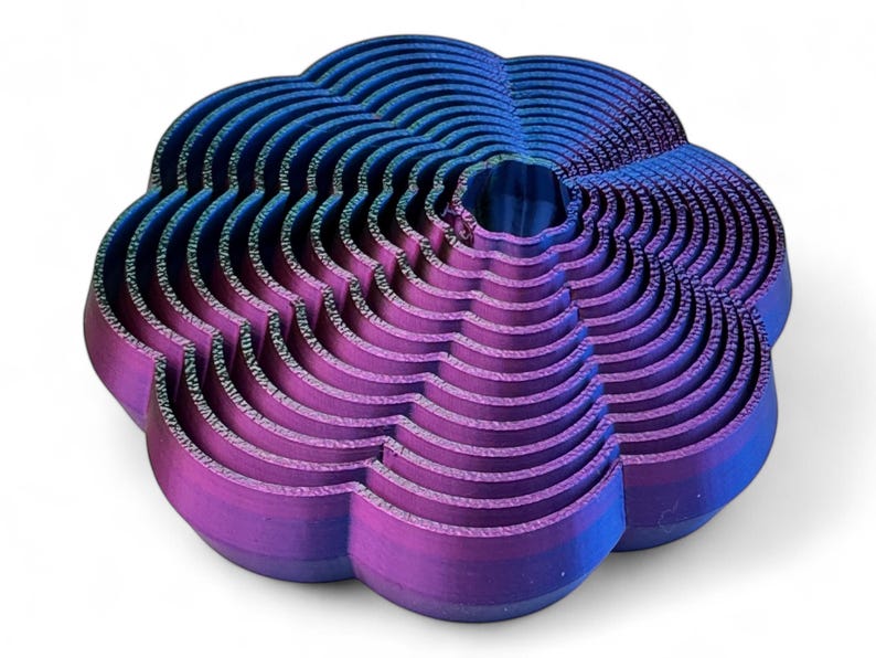 May include: A 3D-printed, abstract sculpture in shades of blue and purple. The object has a layered, wave-like design, with a central opening. The colour gradient shifts from blue at the top to purple at the bottom. The sculpture is on a white background.
