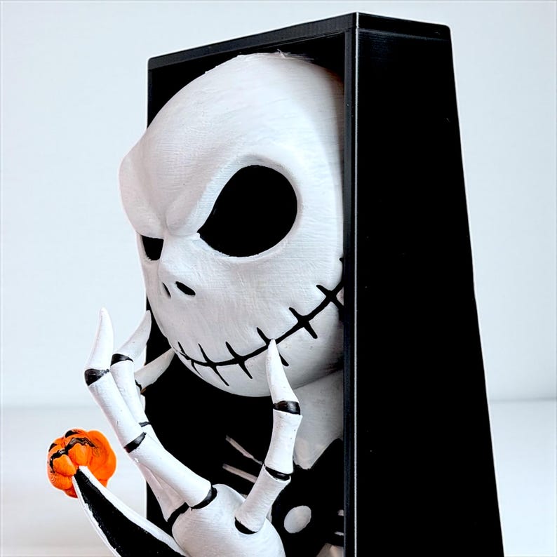 May include: A white Jack Skellington figurine with black stitched mouth and eye sockets, holding a small orange pumpkin. The figurine is set against a black background, creating a striking contrast. The character is from the movie "The Nightmare Before Christmas".