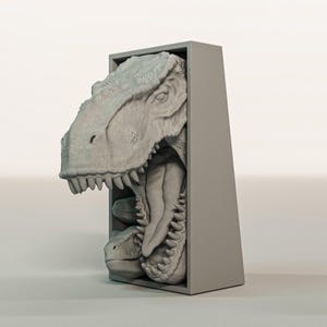 K&ouml;nnte beinhalten: Eine graue, dreidimensionale Skulptur eines Tyrannosaurus Rex-Kopfes, der aus einem rechteckigen Rahmen herausragt. Das Maul des Dinosauriers ist ge&ouml;ffnet und zeigt scharfe Z&auml;hne und ein detailliertes Inneres. Die Skulptur ist in einem neutralen Grauton gehalten.