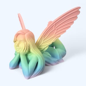May include: A rainbow-colored fairy figurine with wings outstretched, lying on its side with its head resting on its hands. The fairy has long hair and a delicate face.