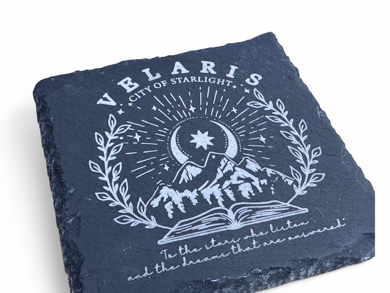 Peut inclure: Un dessous de verre en ardoise noire avec un motif blanc repr&eacute;sentant une lune croissante, une &eacute;toile, des montagnes et un livre ouvert. Le texte "VELARIS CITY OF STARLIGHT" et "To the stars who listen and the dreams that are answered" est &eacute;galement inclus dans le motif.