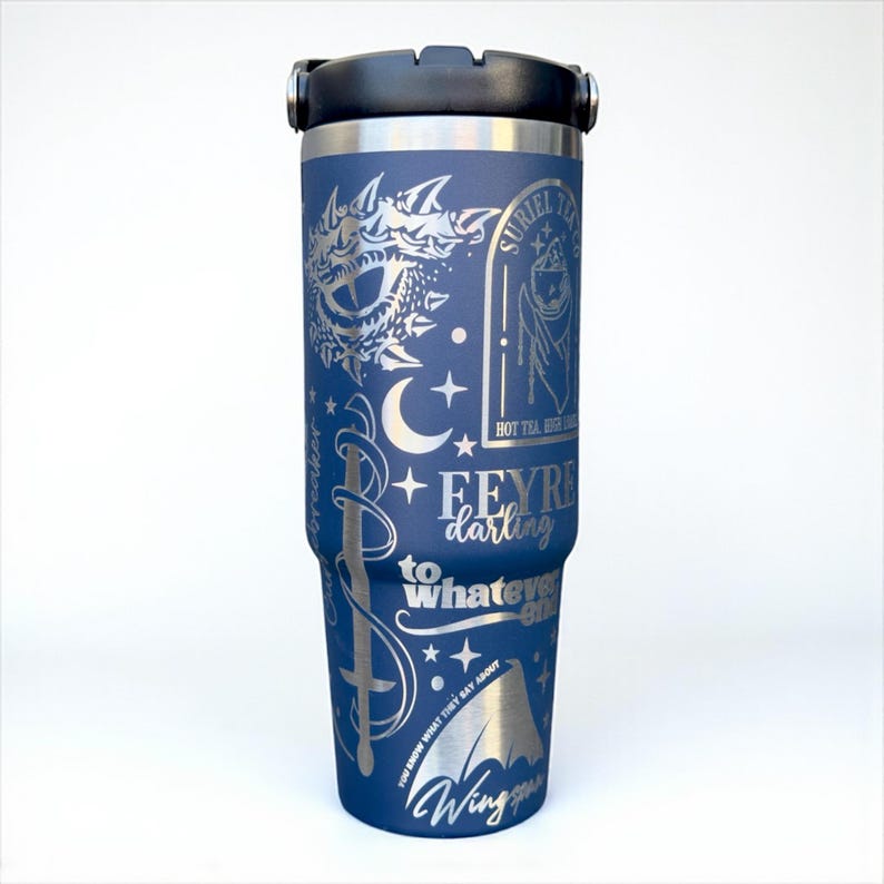 May include: A navy blue insulated travel mug with a black lid and silver etched designs. The mug features text and illustrations, including the words "Feyre darling" and "Wing". The design includes a sword, moon, stars, and a dragon.