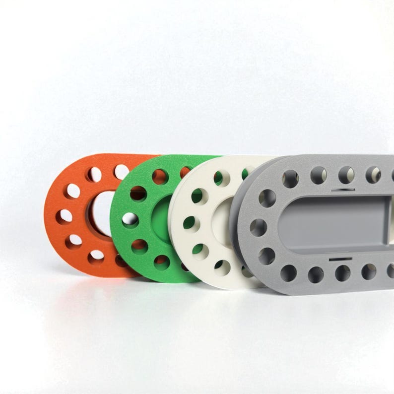 May include: Four colorful, oval-shaped objects with multiple circular holes. The objects are in shades of orange, green, white, and gray. The gray object has a rectangular section. The objects are arranged in a row against a white background.