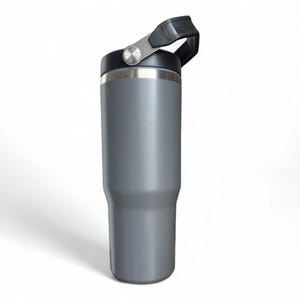 May include: A grey insulated tumbler with a black lid and handle. The stainless steel rim and handle hardware provide a metallic accent. The tumbler is designed to keep beverages cold or hot. The handle is attached to the lid with a hinge.