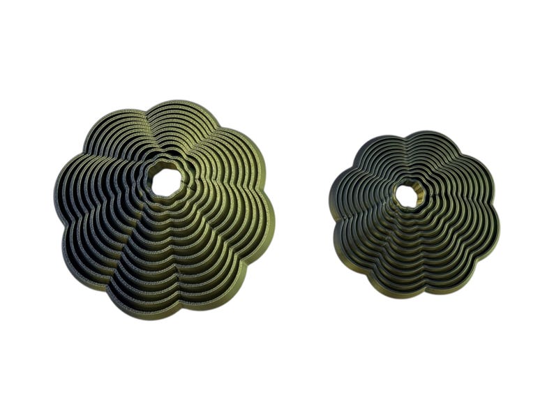May include: Two olive-green, flower-shaped decorative objects. The larger one has a diameter of approximately 15 cm, while the smaller one is about 10 cm across. Both have a central hole and a layered, wavy design.
