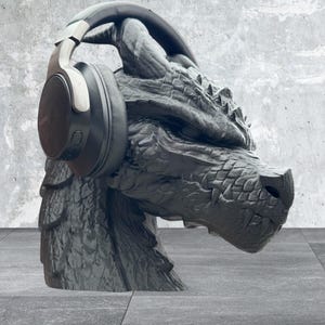 K&ouml;nnte beinhalten: Eine schwarze Drachen-Skulptur mit schwarzen Over-Ear-Kopfh&ouml;rern.