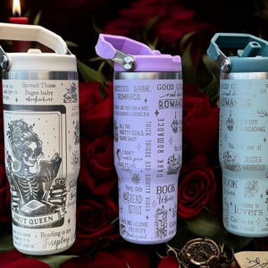 May include: Three stainless steel tumblers with different designs. The white tumbler features a skeleton reading a book with the text "Spread Those Pages Baby" and "Smut Queen". The purple tumbler features a dark romance theme with the text "Dark Romance" and "Book Lovers". The blue tumbler features a dark romance theme with the text "Good Girls Read Bad Romance" and "Trigger Warnings".