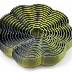 May include: An abstract sculpture in olive green and dark grey, resembling a flower. The piece is composed of concentric, wavy layers, creating a textured surface. The design is modern and artistic, with a unique, layered aesthetic.
