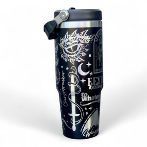 May include: Black insulated travel mug with a black lid and handle. The mug has silver etched designs including a sword, crescent moons, stars, and text that reads "Feyre darling to whatever".