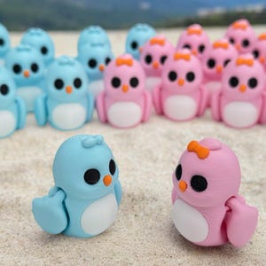 May include: A group of small, hand-painted figurines of penguins in blue and pink colors. The penguins are arranged in two rows, with the blue penguins in the front row and the pink penguins in the back row.