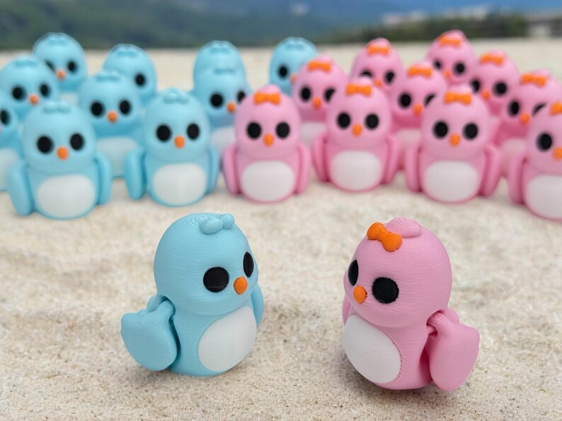 May include: A group of small, hand-painted figurines of penguins in blue and pink colors. The penguins are arranged in two rows, with the blue penguins in the front row and the pink penguins in the back row.