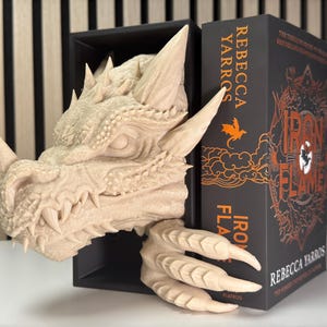 May include: A beige dragon head bookend with a book titled "Iron Flame" by Rebecca Yarros. The book is black with orange text and illustrations.