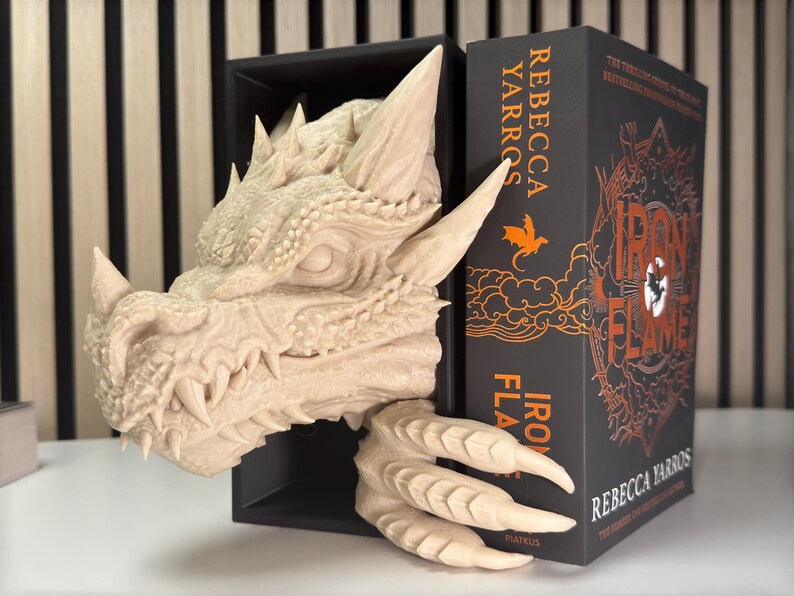 May include: A beige dragon head bookend with a book titled "Iron Flame" by Rebecca Yarros. The book is black with orange text and illustrations.