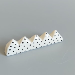 May include: White ceramic chopstick rest with a black polka dot pattern shaped like a row of mountains.