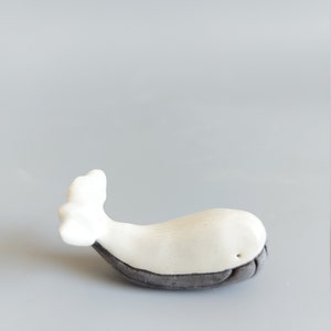 May include: A white ceramic whale figurine with a gray underside. The whale is lying on its side with its tail in the air.