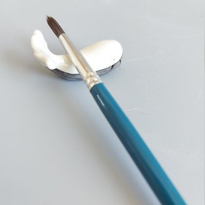 May include: A white ceramic whale brush holder with a blue paintbrush resting on top.