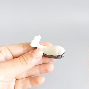May include: A small white ceramic whale figurine with a gray tail and a black eye. The whale is about 2 inches long.