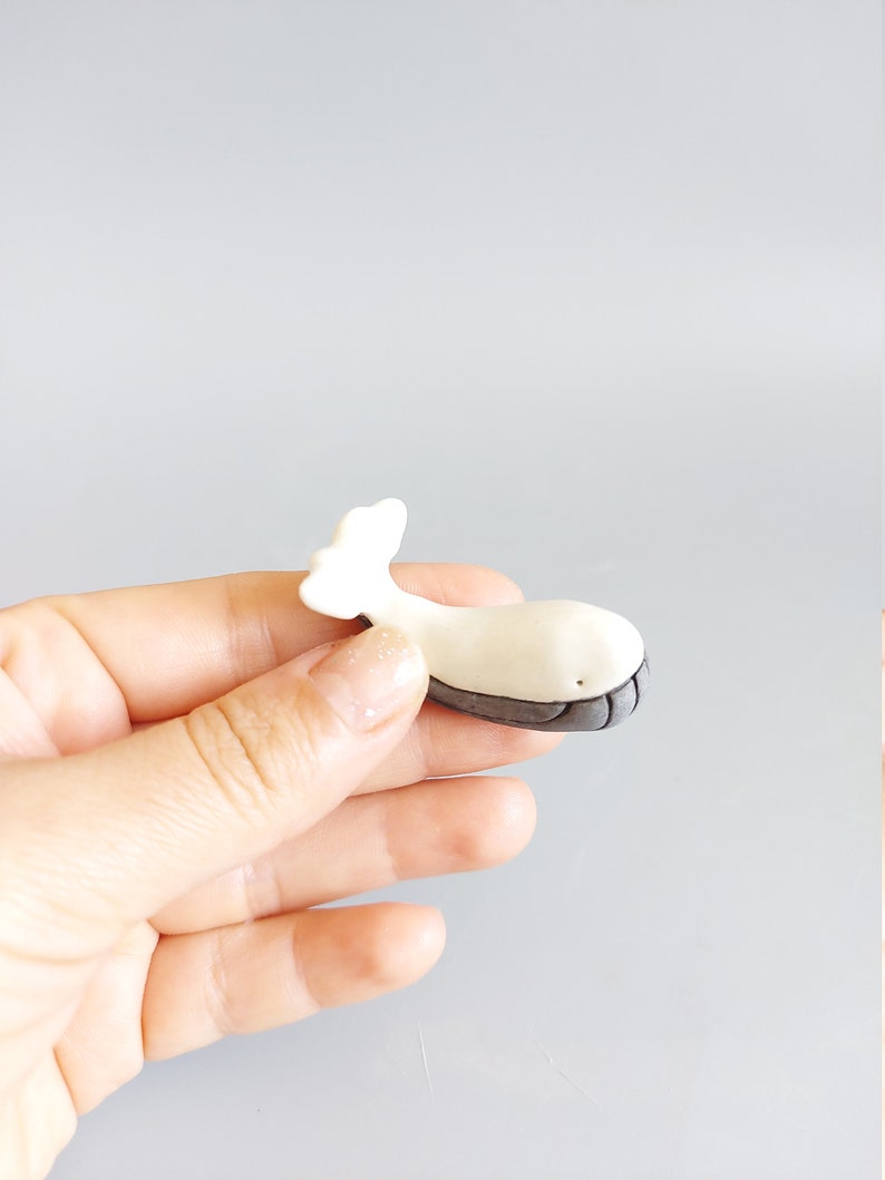 May include: A small white ceramic whale figurine with a gray tail and a black eye. The whale is about 2 inches long.