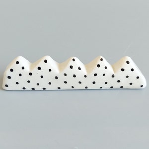 May include: White ceramic chopstick rest with a black polka dot pattern. The rest is shaped like a row of mountains.