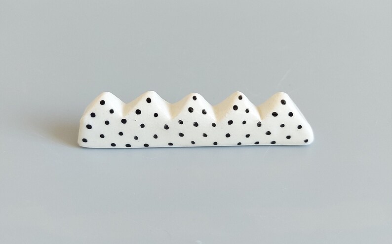 May include: White ceramic chopstick rest with a black polka dot pattern. The rest is shaped like a row of mountains.