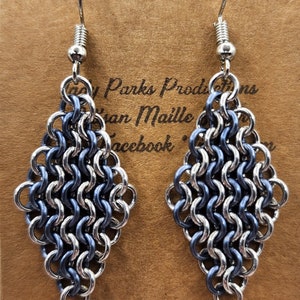 May include: A pair of silver and blue diamond-shaped earrings made of chainmail. The earrings are hanging from silver hooks.