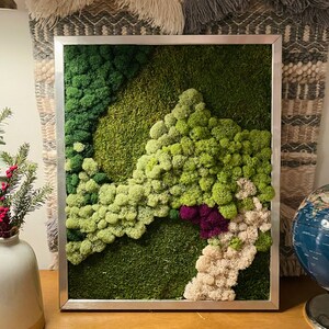 May include: A framed moss wall art piece with a variety of green, white, and purple moss arranged in a landscape design.