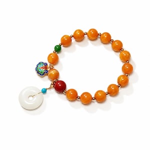 May include: A beaded bracelet featuring round orange amber-colored beads separated by small gold-tone spacers. The bracelet includes a red bead, a green bead, a small colorful enamel charm, and a large white circular jade-like pendant charm.