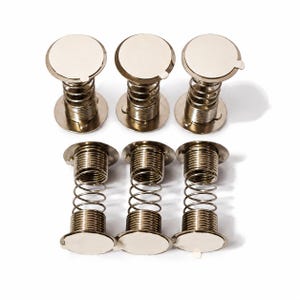 May include: Six silver-toned metal spring-loaded mechanisms arranged in two rows. Each unit features a cylindrical coil spring positioned between two flat, circular end plates with a smooth, reflective finish on the outer surfaces.