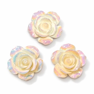 May include: Three individual rose-shaped ornaments featuring a cream-colored base with a distinct iridescent, pearlescent finish that reflects subtle hints of pink, blue, and yellow light across the curved, layered petals of each flower.