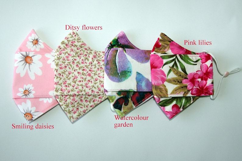 Puede incluir: Cuatro mascarillas de tela diferentes con patrones florales. Las mascarillas son de color rosa, blanco y verde con varios dise&ntilde;os florales, incluyendo margaritas, lirios y un patr&oacute;n de jard&iacute;n de acuarela. Las mascarillas est&aacute;n etiquetadas con sus nombres: Smiling daisies, Ditsy flowers, Watercolor garden y Pink lilies.