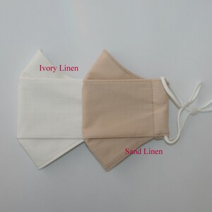 May include: A reversible face mask made of linen fabric. One side is ivory linen and the other side is sand linen. The mask has white elastic ear loops.