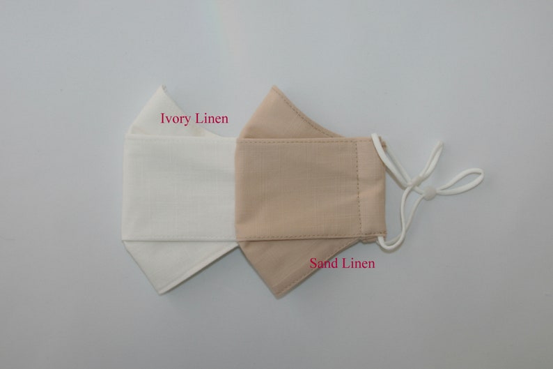 May include: A reversible face mask made of linen fabric. One side is ivory linen and the other side is sand linen. The mask has white elastic ear loops.
