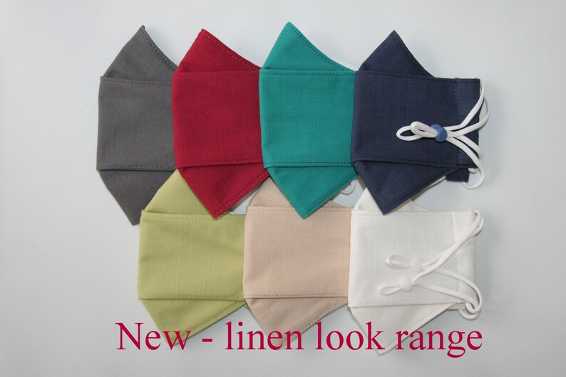 May include: Seven face masks in different colors, including gray, red, teal, navy, light green, beige, and white. The masks are made of a linen-like fabric and have adjustable ear loops. "New - linen look range" is written in red text at the bottom of the image.