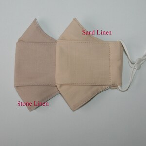 May include: Two beige linen face masks, one labeled "Stone Linen" and the other "Sand Linen".