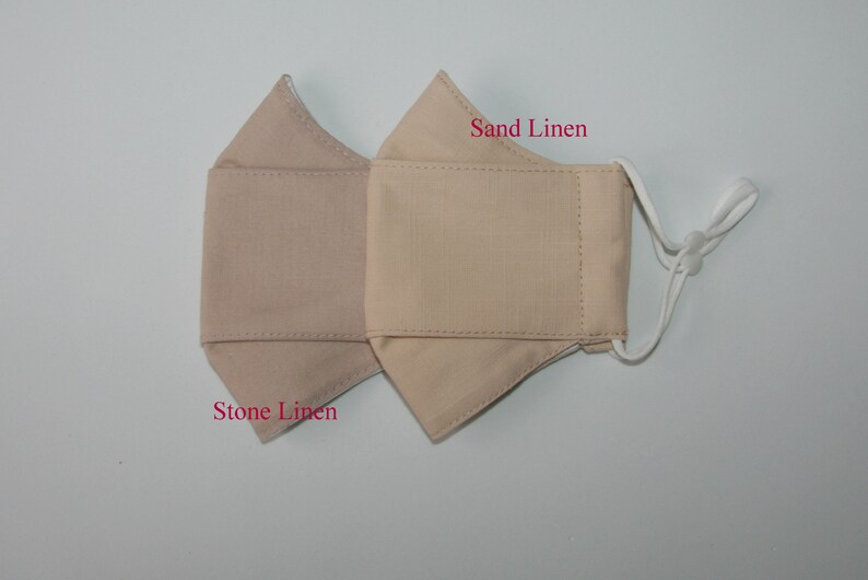 May include: Two beige linen face masks, one labeled "Stone Linen" and the other "Sand Linen".