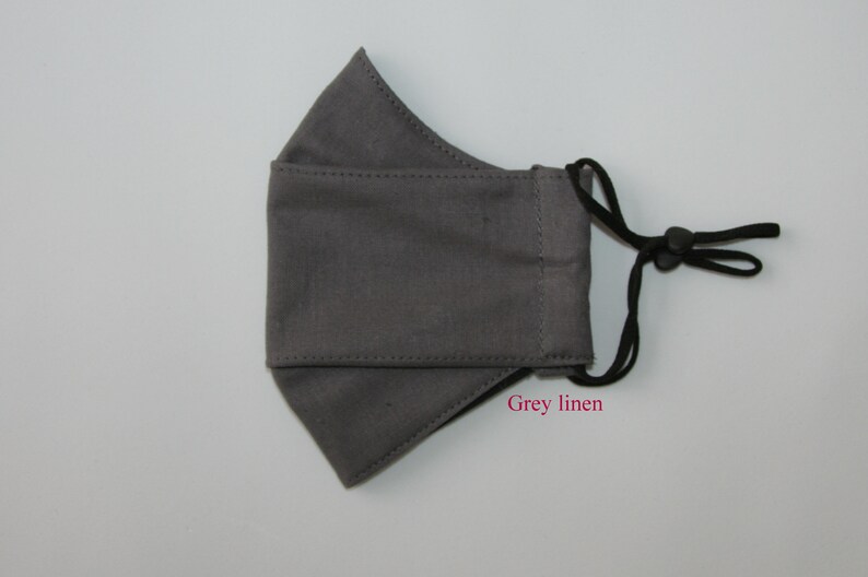 May include: A gray linen face mask with black adjustable straps. The mask has a simple design and is made of a soft, breathable fabric.  Grey linen.