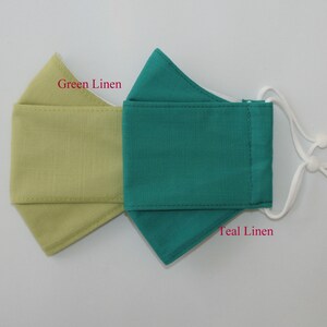 May include: Two fabric face masks, one green linen and one teal linen. The masks are sewn with white thread and have white elastic ear loops.