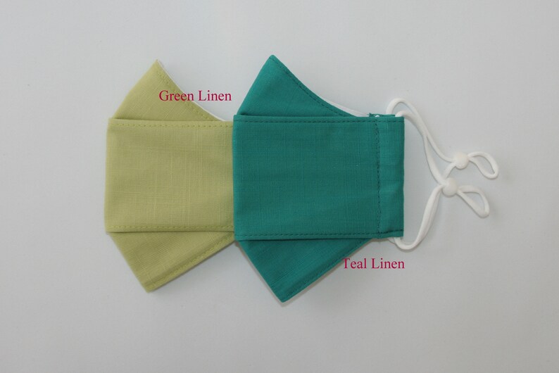 May include: Two fabric face masks, one green linen and one teal linen. The masks are sewn with white thread and have white elastic ear loops.
