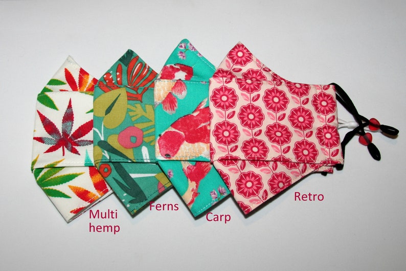Puede incluir: Cuatro mascarillas de tela diferentes con varios patrones. Las mascarillas est&aacute;n dobladas y dispuestas en fila. Los patrones son: multi c&aacute;&ntilde;amo, helechos, carpa y retro.